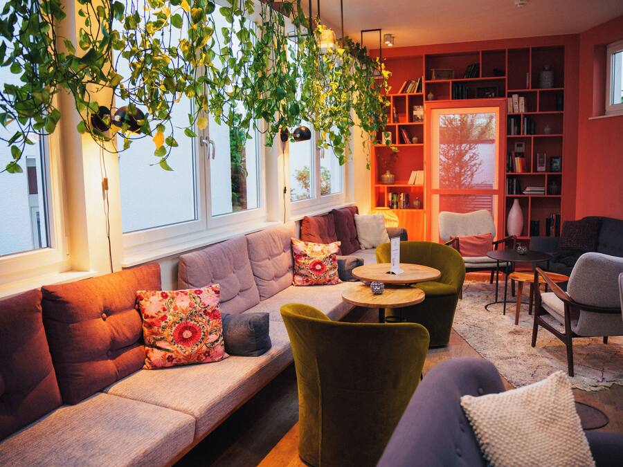 Ein gemütliches Wohnzimmer mit einer Couch, Sesseln, einem Couchtisch und einem Bücherregal, das mit Büchern und Dekoration gefüllt ist.