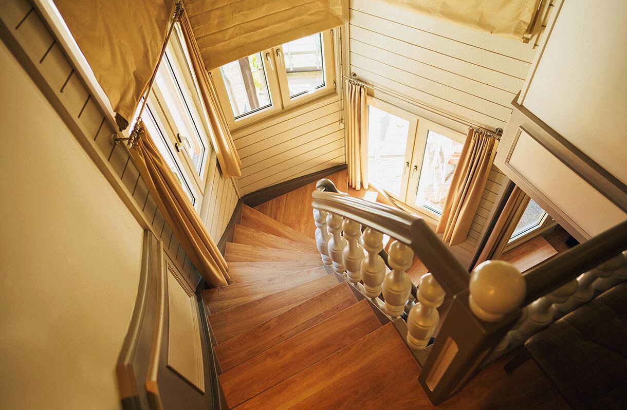 Uma escada de madeira com corrimão, que dá acesso a um quarto com janela e porta.
