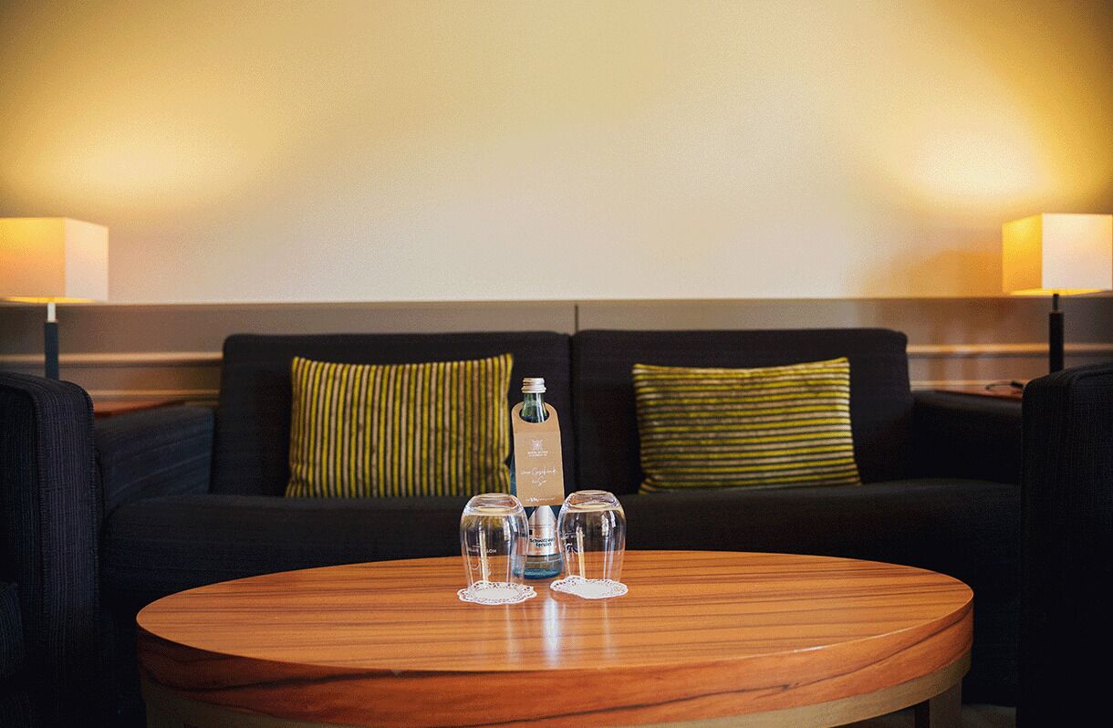 A room with a round wooden table, two black sofas, and a bottle of water.