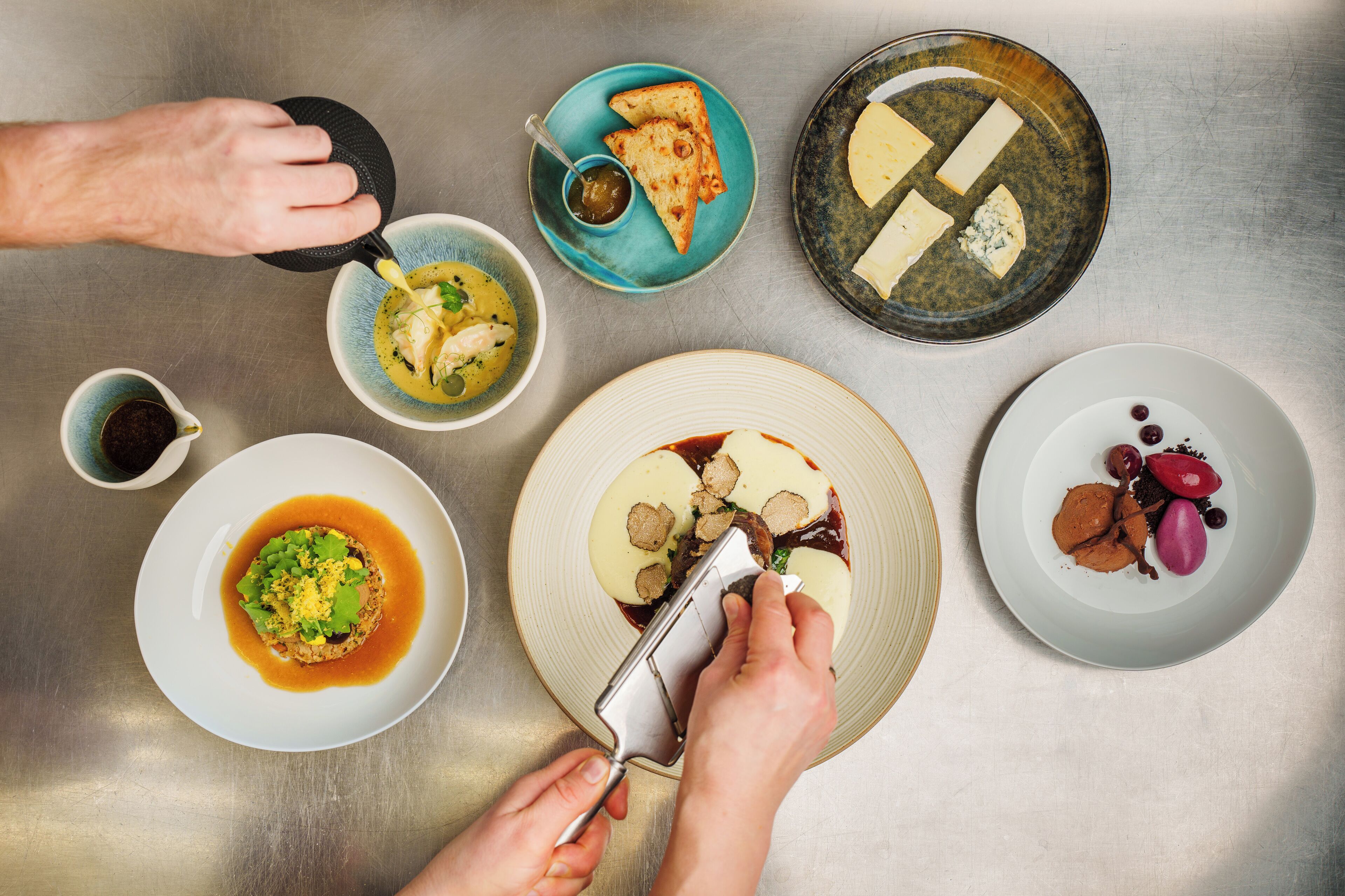 A top-down view of a dining table with various dishes, including a soup, a plate with meatballs, and a plate with cheese and olives.