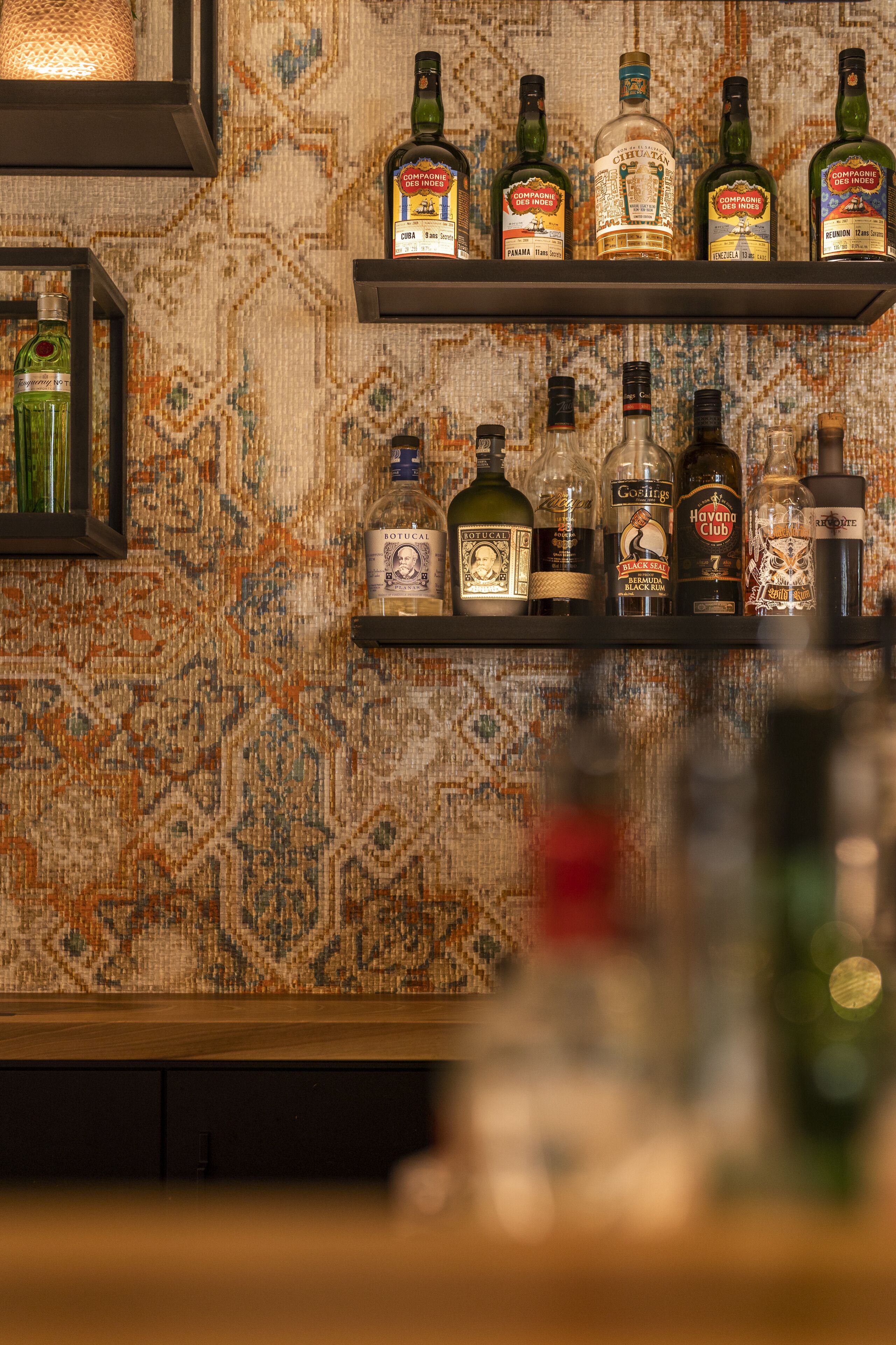 Shelves with various liquor bottles against a patterned wall.