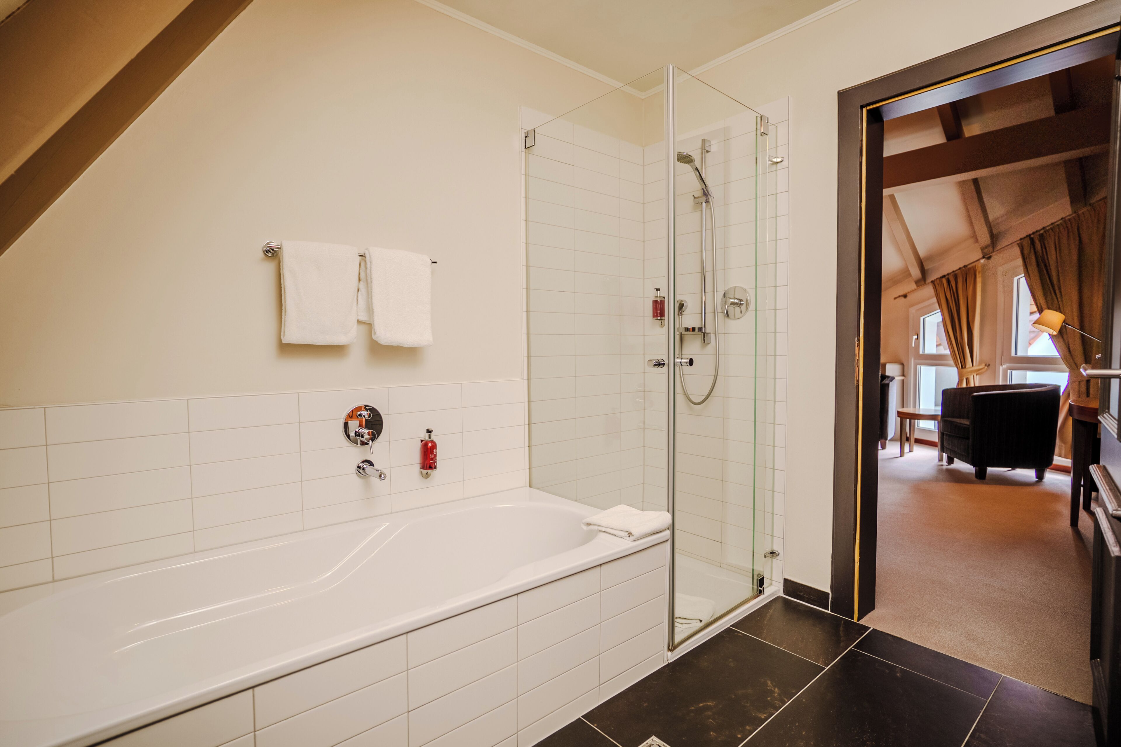 Ein modernes Badezimmer mit Badewanne, einer Duschkabine aus Glas und einer sichtbaren Tür zu einem weiteren Raum.