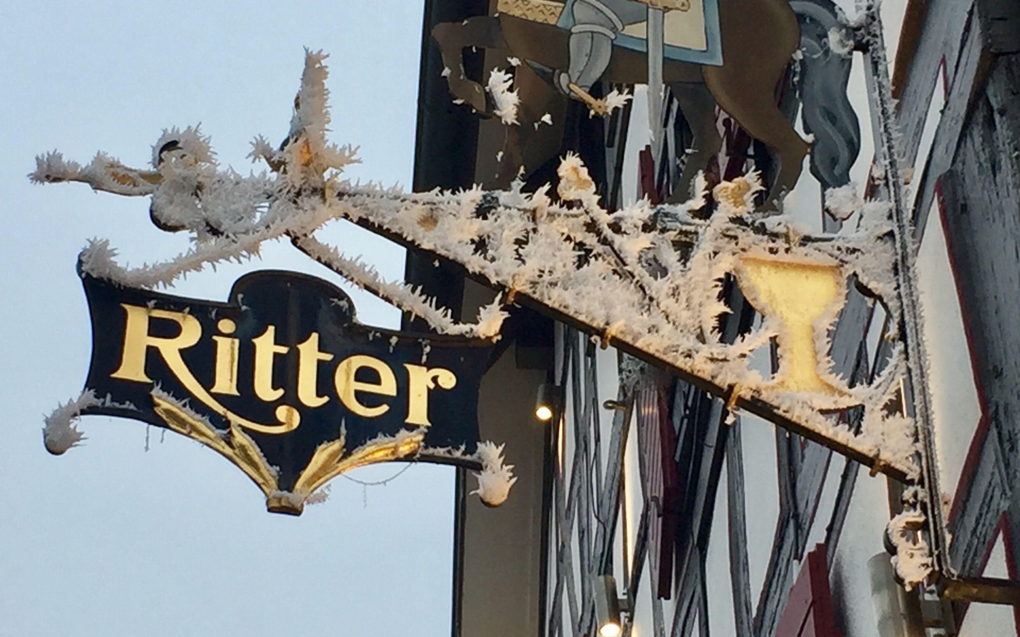 A sign with the word 'Ritter' in gold lettering on a black background, surrounded by intricate, frost-like decorations.
