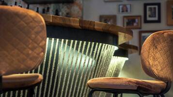 Una zona de bar con mostrador de madera y dos sillones tapizados.