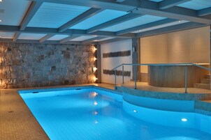 Una piscina interior moderna con paredes de piedra, barandilla de cristal e iluminación empotrada.