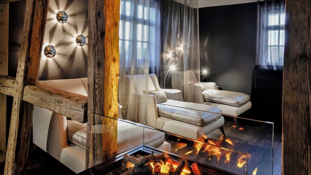 A modern living room with a fireplace, wooden beams, and a glass coffee table. - Hotel Ritter Durbach (Durbach)