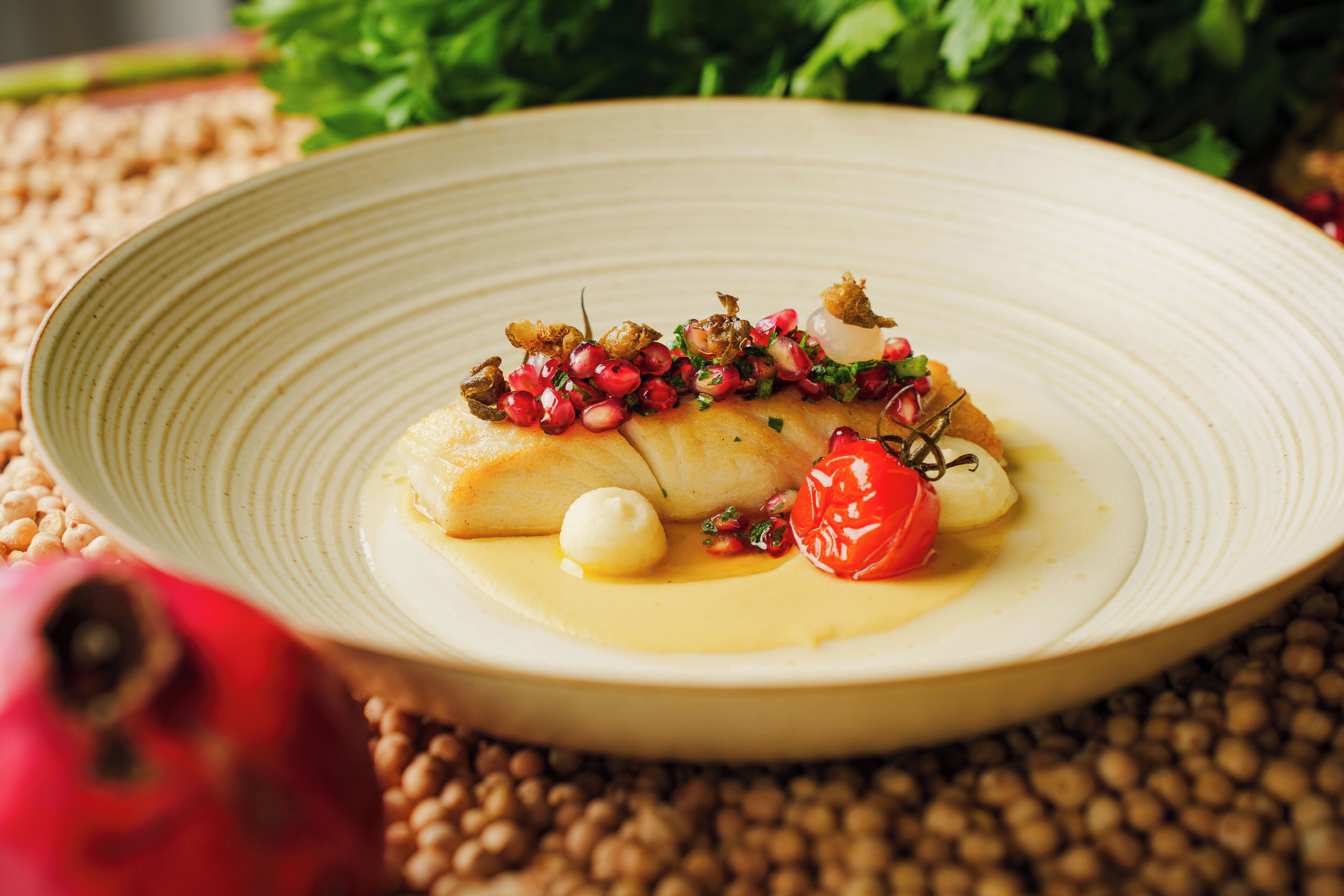 A plate of food with a white sauce, pomegranate seeds, and a cherry tomato.