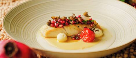 A plate of food with a white sauce, pomegranate seeds, and a cherry tomato.