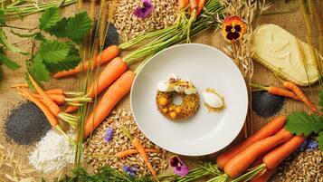 A plate with a food item, surrounded by carrots, grains, and flowers on a burlap background.