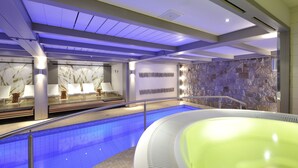 Una piscina interior moderna con pared de piedra y zona de relajación con sillones y camilla de masaje.