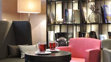 A cozy seating area with a sofa, a small round table with two cups of tea, and a bookshelf filled with books and decorative items.