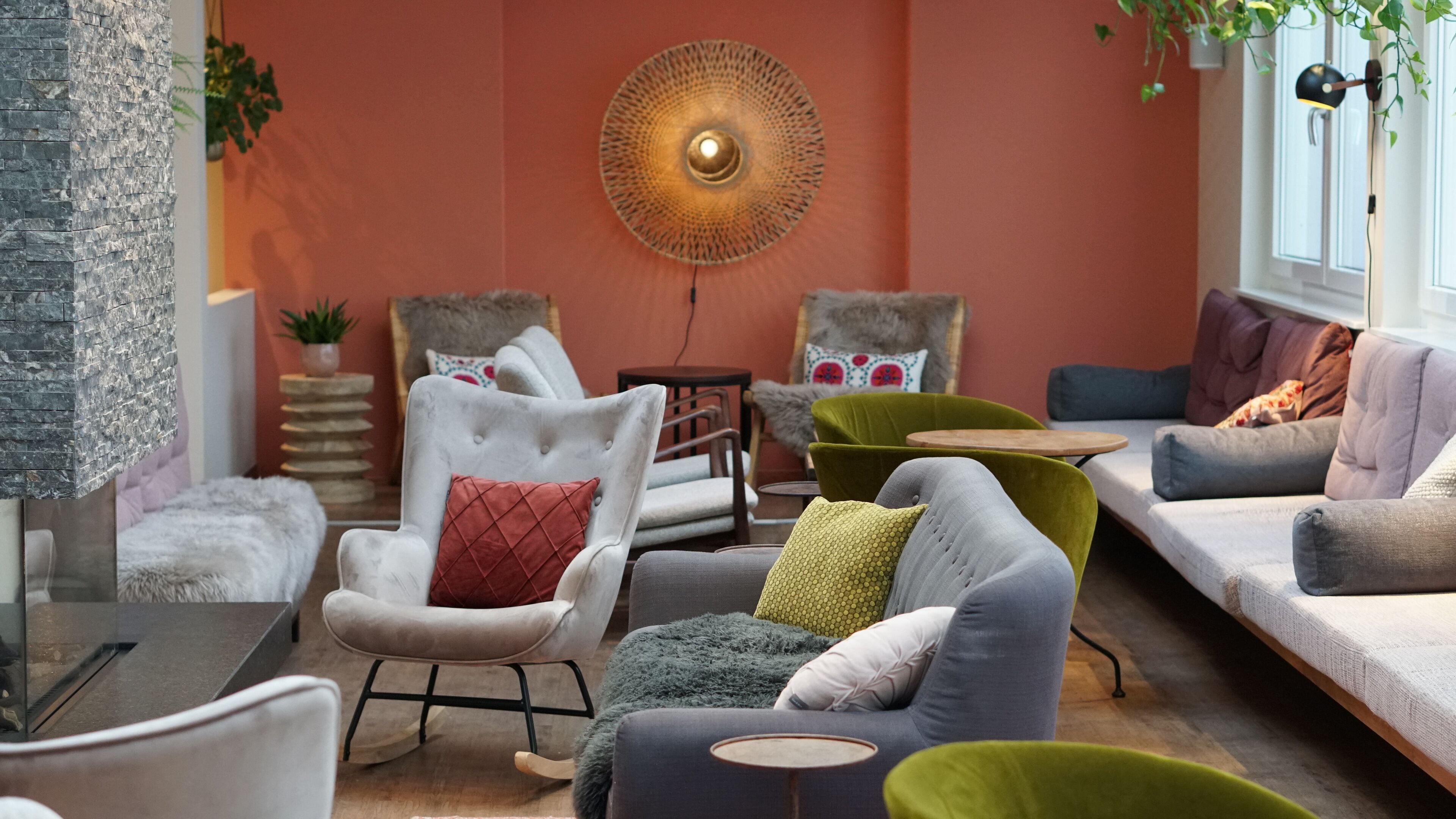Ein modernes Wohnzimmer mit einer Wand aus Stein, einer runden Deckenleuchte und unterschiedlichen Sitzgelegenheiten, darunter ein Sofa, Sessel und ein grüner Sessel.