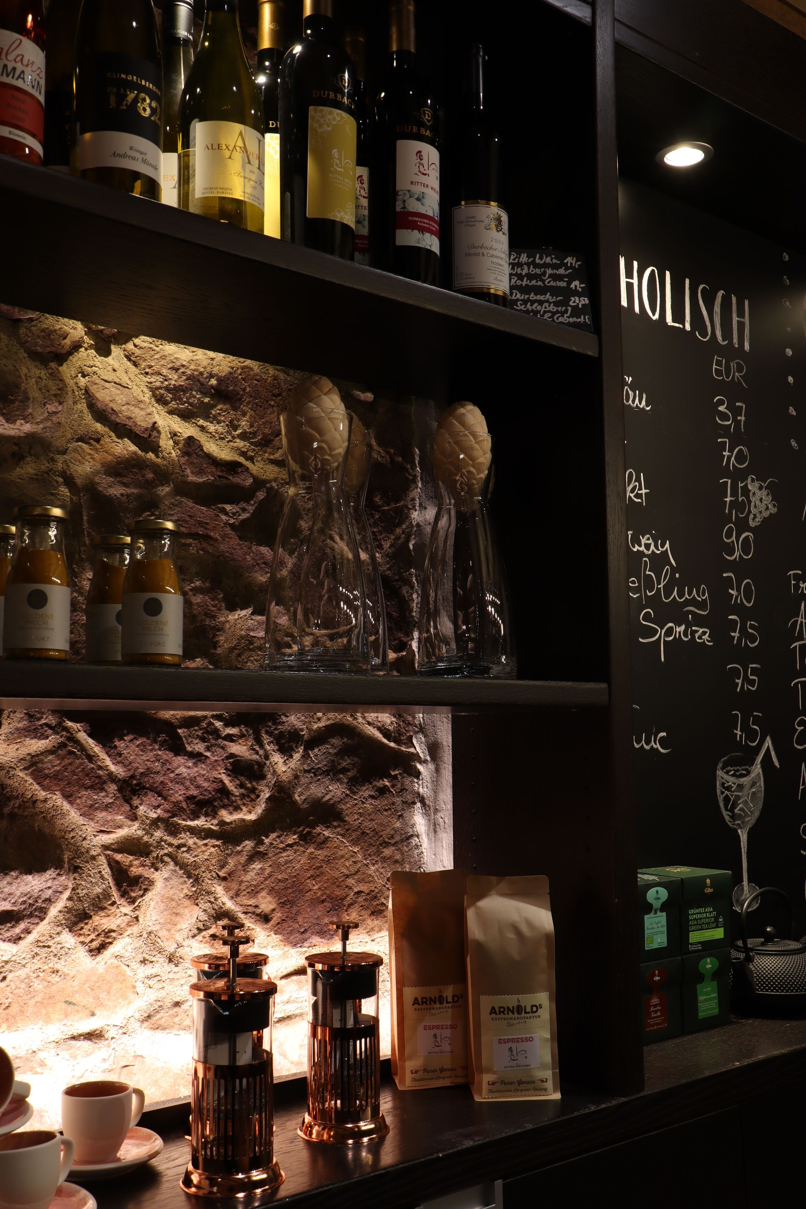 A bar area with shelves of wine bottles, a chalkboard menu, and coffee-making equipment.