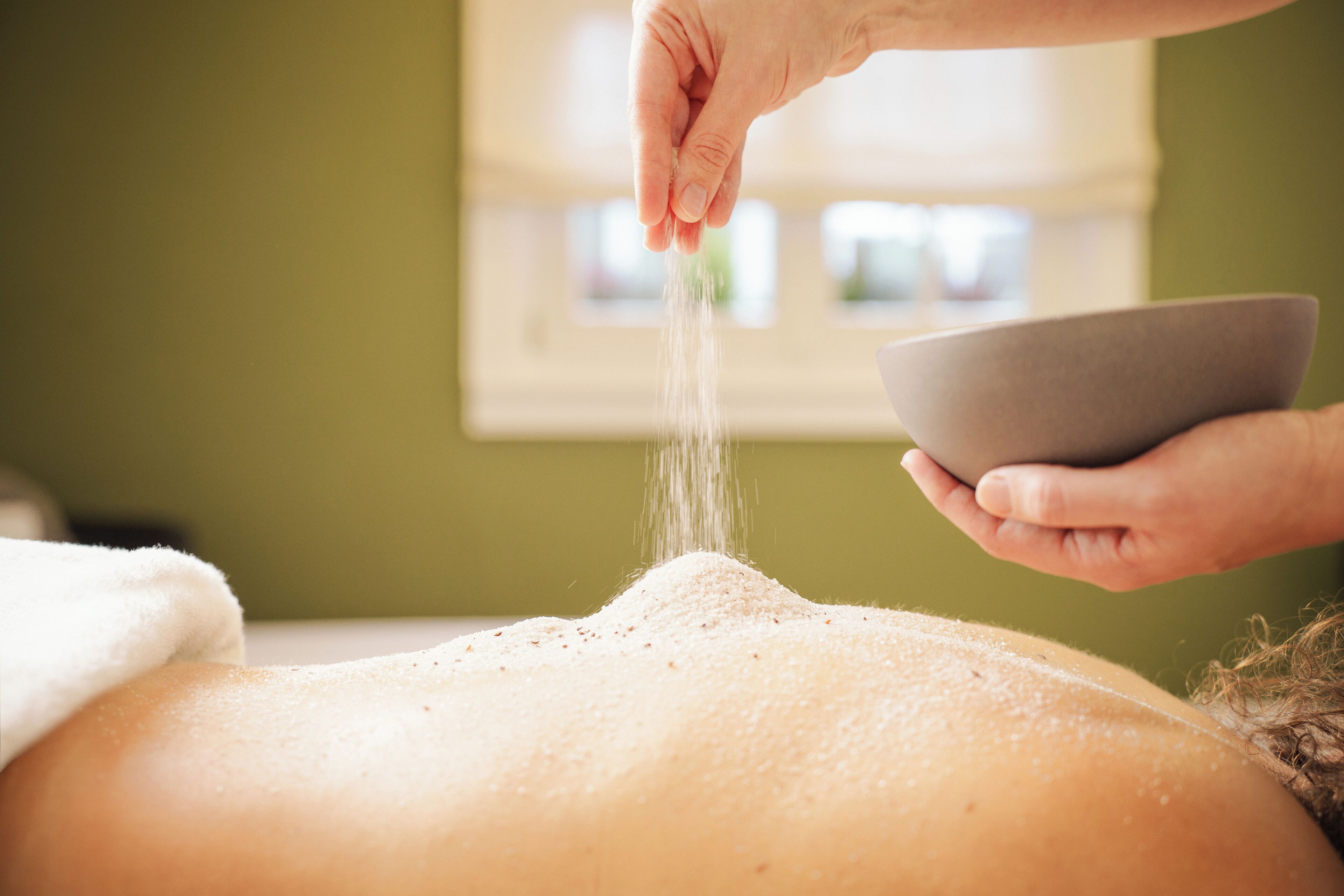 Iemand ontvangt een massage, er wordt zout over de rug gestrooid.