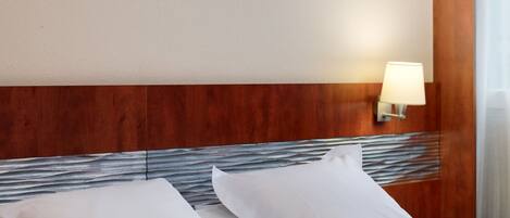 Ein Hotelzimmer mit einem Bett, weißen Leinentüchern, einem gerahmten Landschaftsbild, einer Wandlampe und einem Holzkopfende.