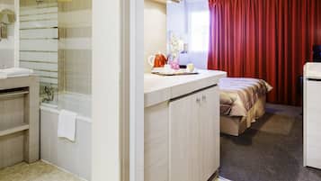 Une chambre d’hôtel avec une salle de bain, un lit, un bureau et une fenêtre avec des rideaux.