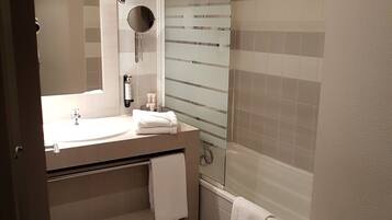 Un baño con lavamanos, espejo, toallero y ducha.