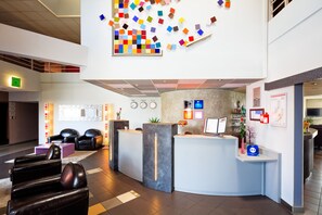 A modern reception area with a curved desk, leather seating, and a colorful abstract art piece on the wall. - Hotel et Residence Octel (Portet-sur-Garonne)