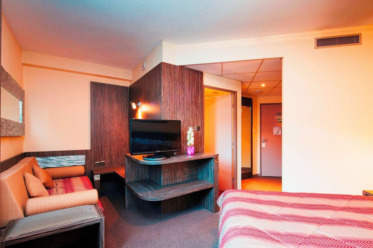 Una habitación de hotel con cama, sofá, televisión y escritorio.