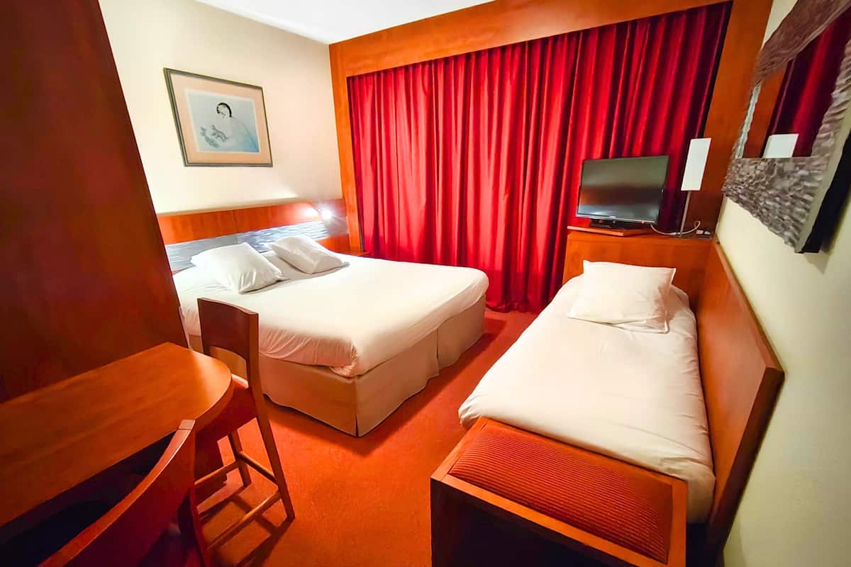 Habitación de hotel con dos camas, un escritorio, una silla, un televisor y una cortina roja.