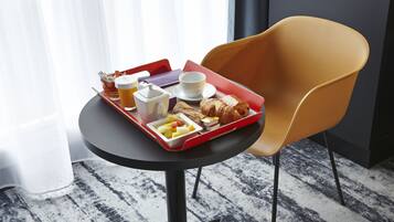 Bandeja de desayuno con cruasanes, fruta y una taza de café sobre una mesa en una habitación de hotel.