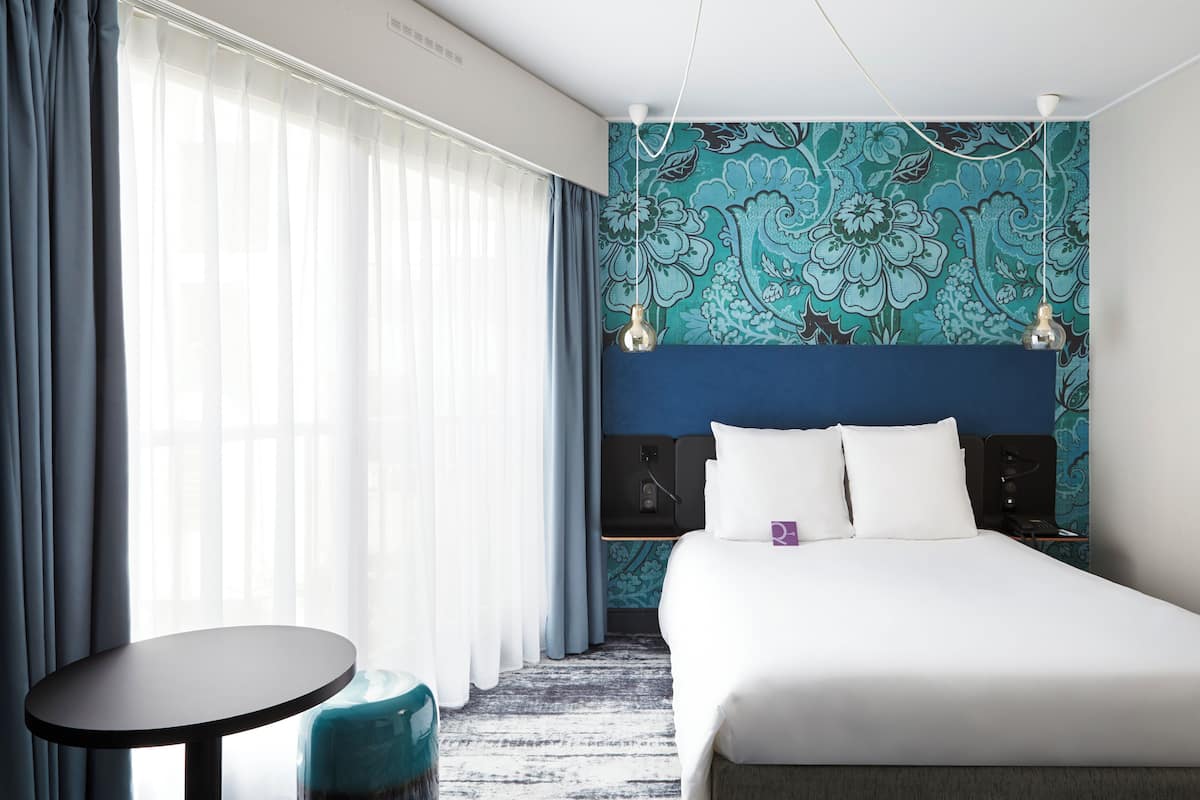 A hotel room with a bed, a round table, and a patterned wall.
