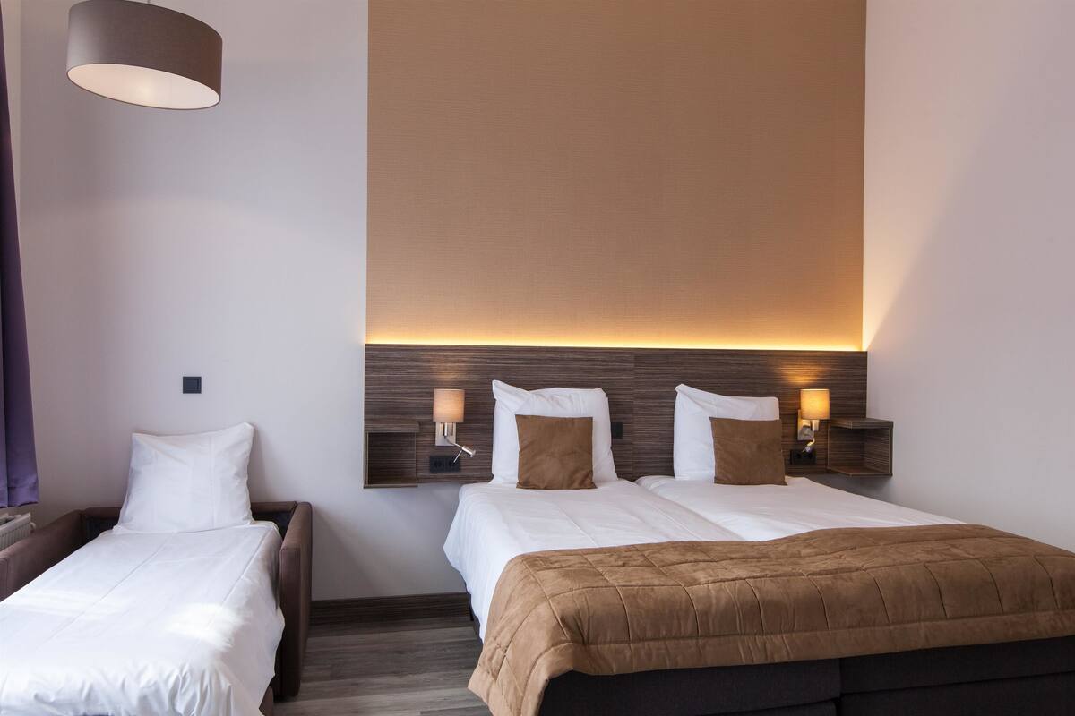 Habitación de hotel con dos camas, cabecero de madera, lámparas de noche e iluminación colgante moderna.