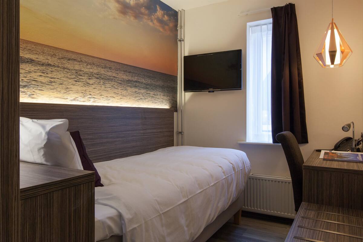 Habitación de hotel con cama, televisión de pantalla plana, escritorio con silla y ventana con cortinas.