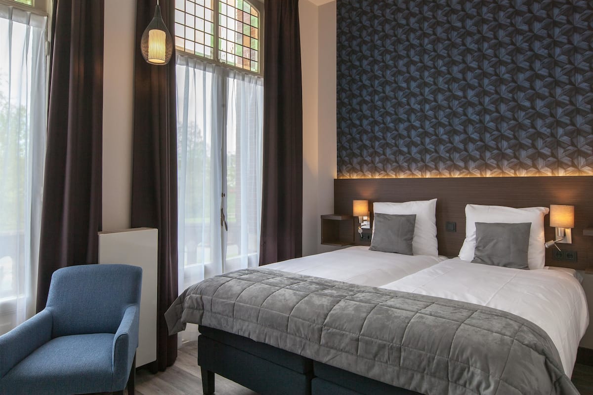Habitación de hotel con una cama grande, una silla, una mesita de noche y una pared con diseño geométrico.