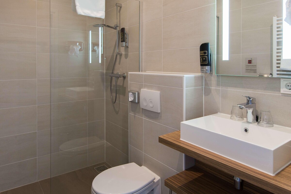 A modern bathroom with a glass shower enclosure, a white toilet, and a wooden vanity with a white sink.