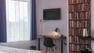 A bedroom with a bed, a desk with a computer monitor, a chair, a bookshelf, and a window with curtains.