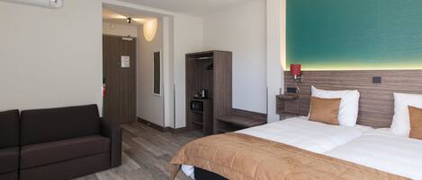 A hotel room with a bed, a sofa, a wardrobe, and a wall-mounted TV.