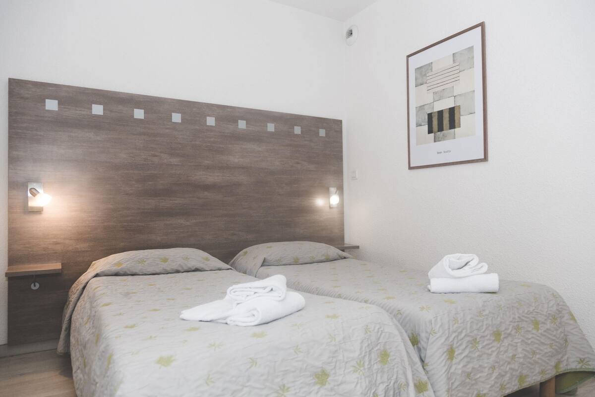 A hotel room with two beds, a wooden headboard, bedside lamps, and a framed artwork on the wall.