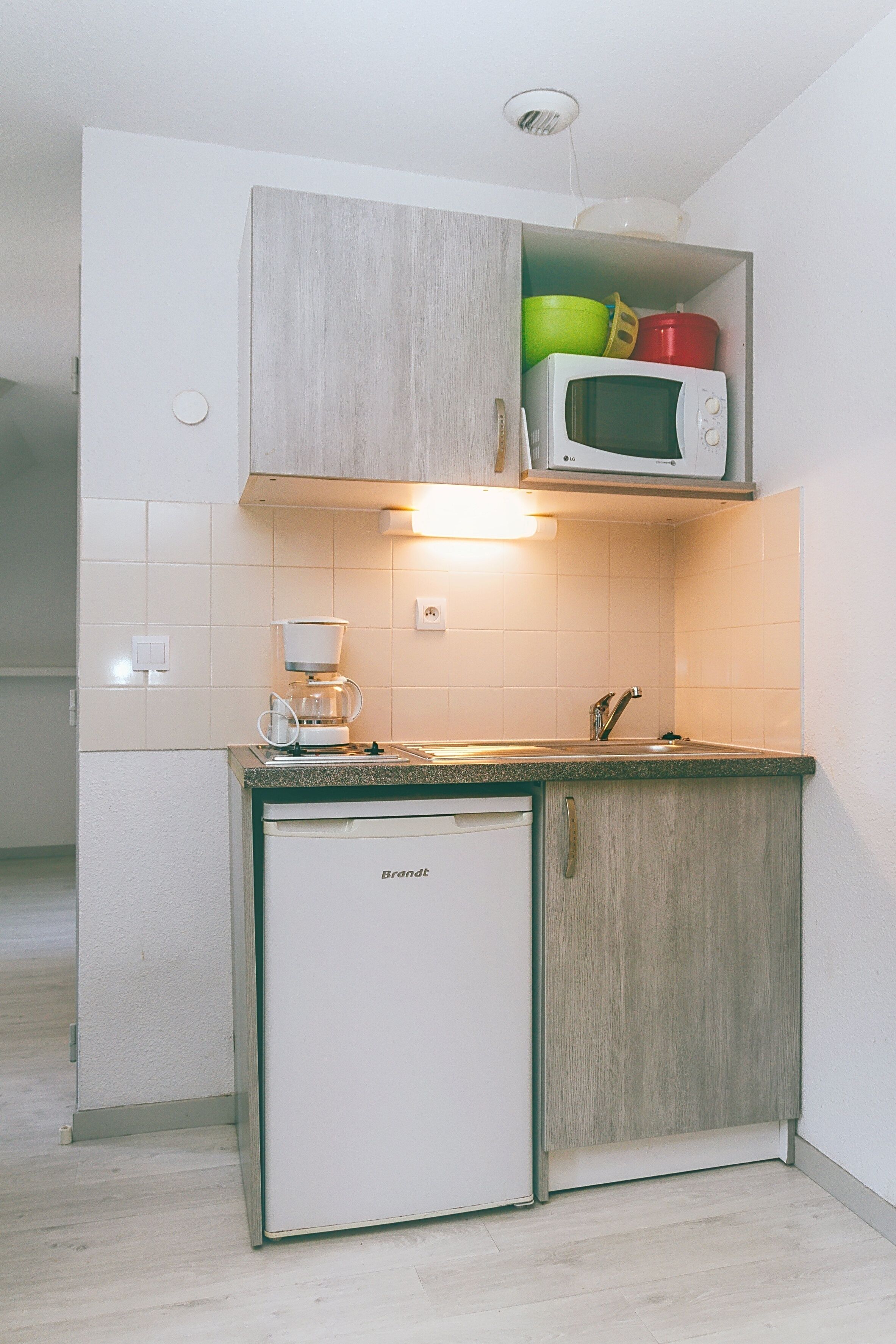 A compact kitchen with a built-in microwave, a coffee maker, and a small refrigerator.