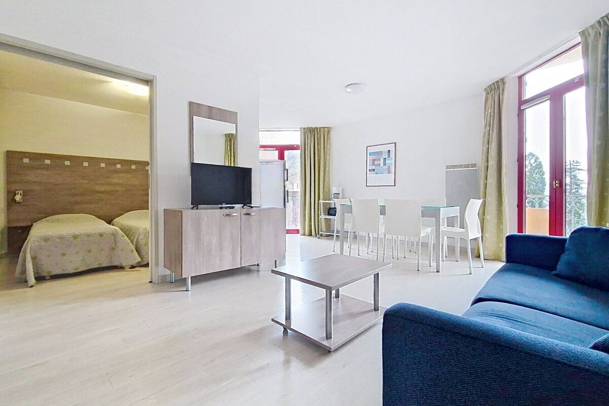 A hotel room with a bed, a TV, a desk, a chair, a sofa, and a dining table.