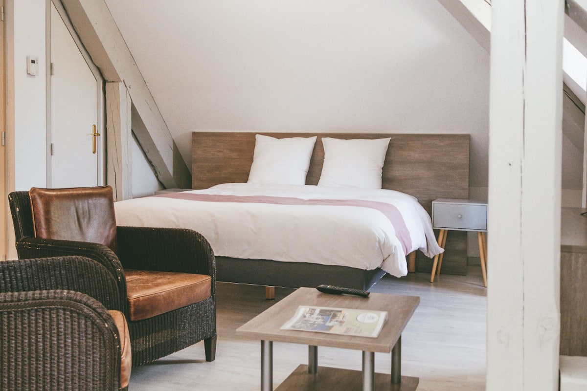 A bedroom with a bed, two wicker chairs, a small table, and a nightstand.