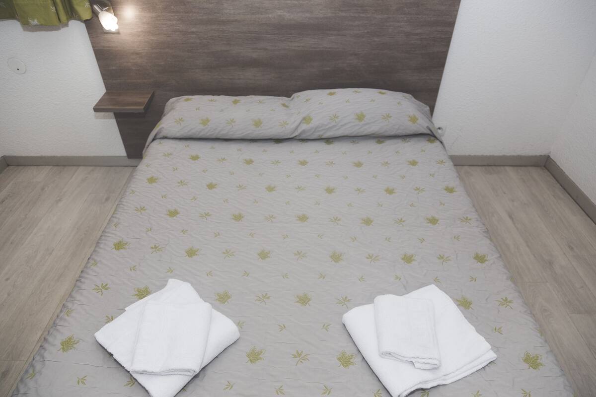 A neatly made bed with a floral-patterned bedspread and two folded white towels on the bed.