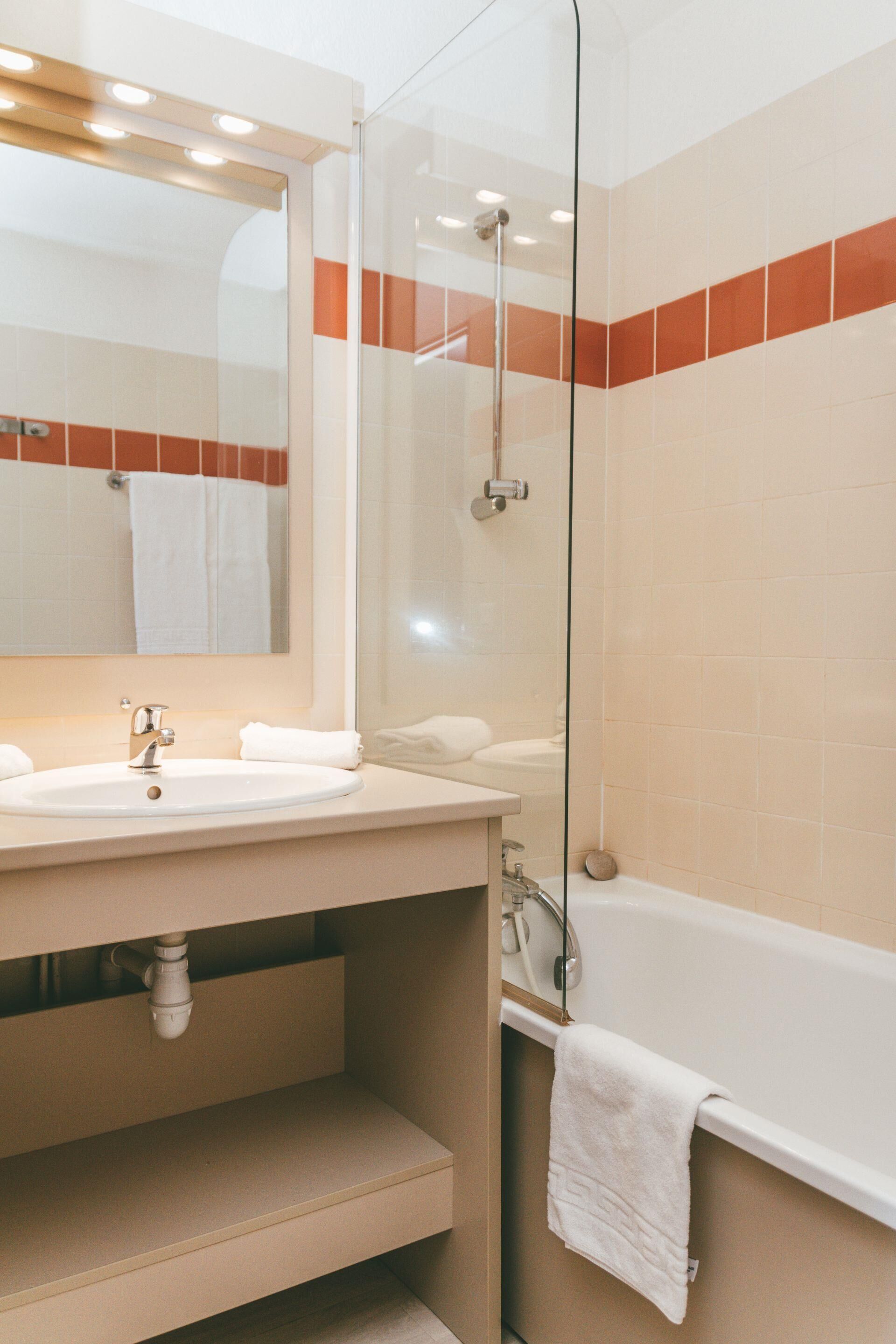 A modern bathroom with a glass-enclosed shower, a sink with a mirror above it, and a bathtub with a towel hanging on the side.