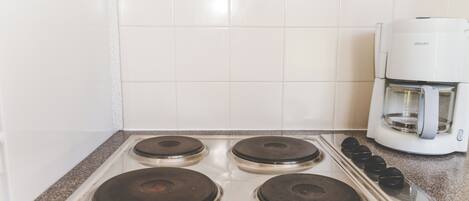 A kitchen with four burners, a coffee maker, and white tiled walls.