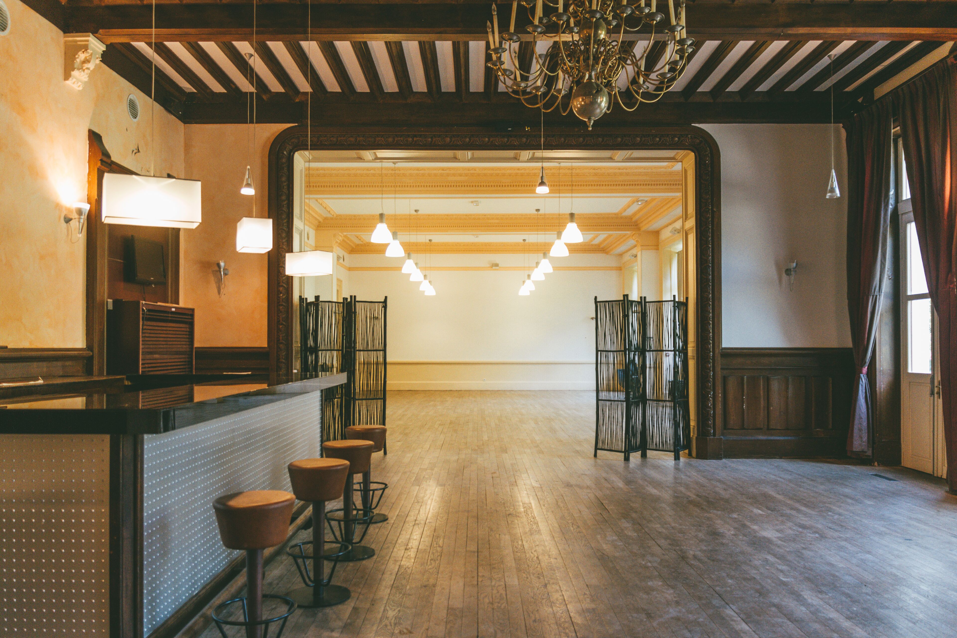 A spacious bar area with wooden flooring, a counter with stools, and pendant lighting.