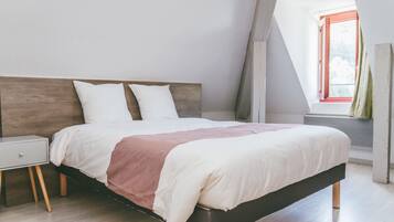 Une chambre moderne avec une tête de lit en bois, un lit simple avec une literie blanche et rose, une table de chevet et une fenêtre donnant sur un paysage verdoyant.