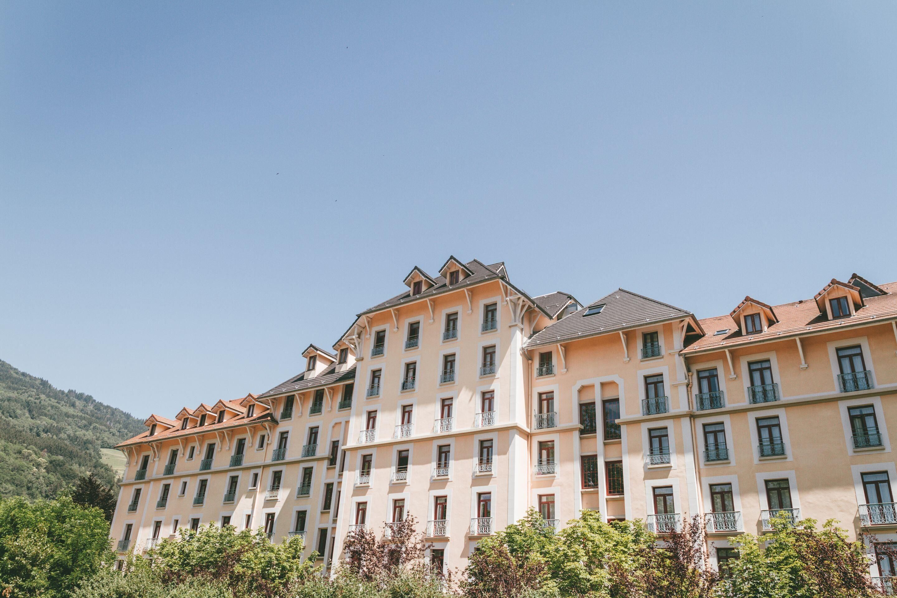 A multi-story hotel with a symmetrical facade, balconies, and a mountainous backdrop.
