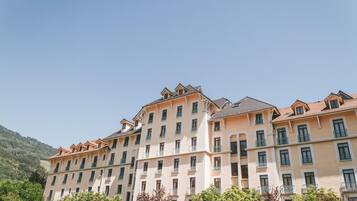 A multi-story hotel with a symmetrical facade, balconies, and a mountainous backdrop.