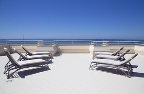A rooftop terrace with two sun loungers and a table, overlooking a clear blue sea. - Hotel Atlantico (Forte dei Marmi)