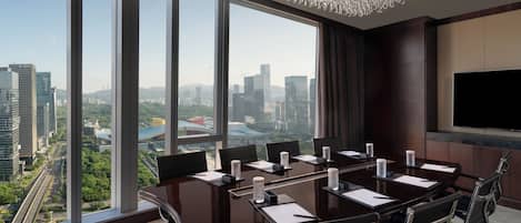A conference room with a large table, chairs, a chandelier, a TV, and a city view.
