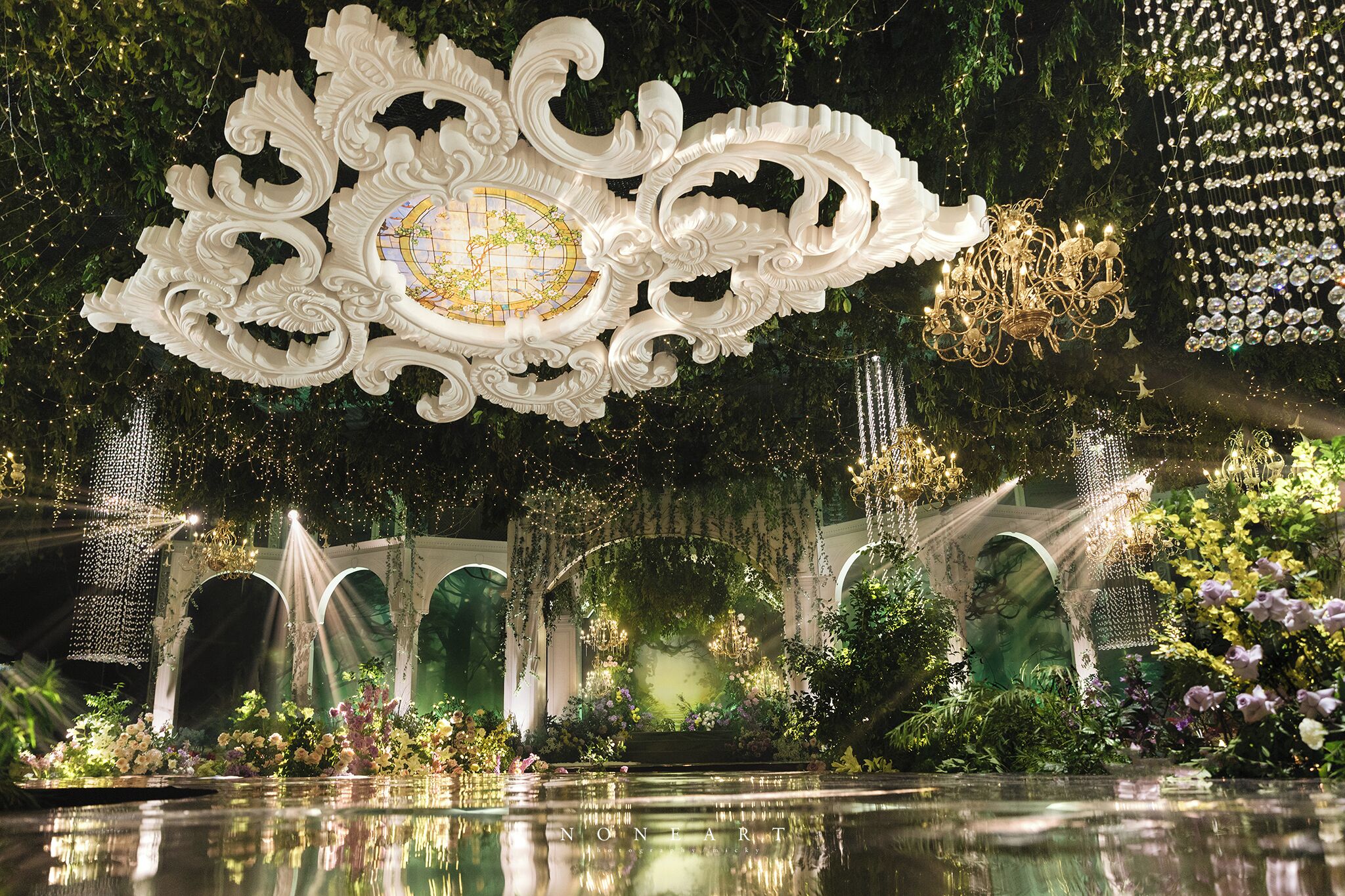 An ornate ceiling with a central globe, a chandelier, and a water feature with plants.