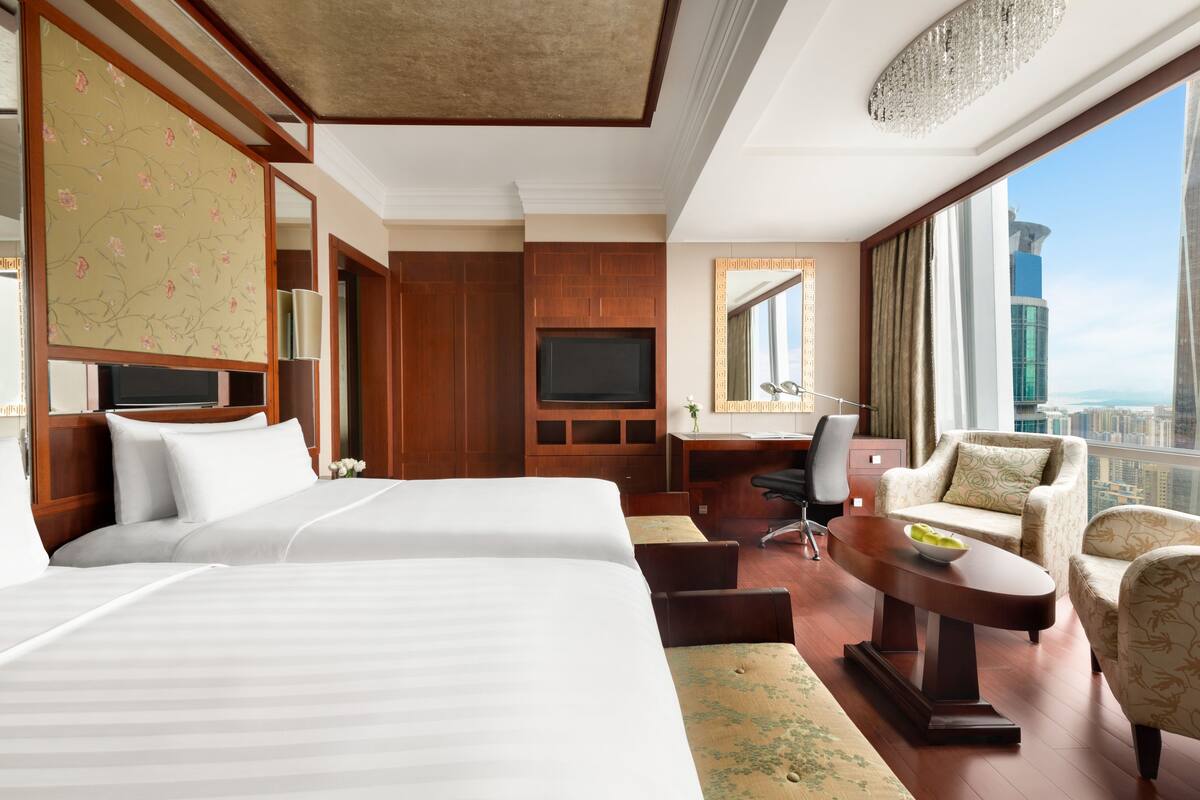 Habitación de hotel con dos camas, un escritorio, una silla y vista a la ciudad.