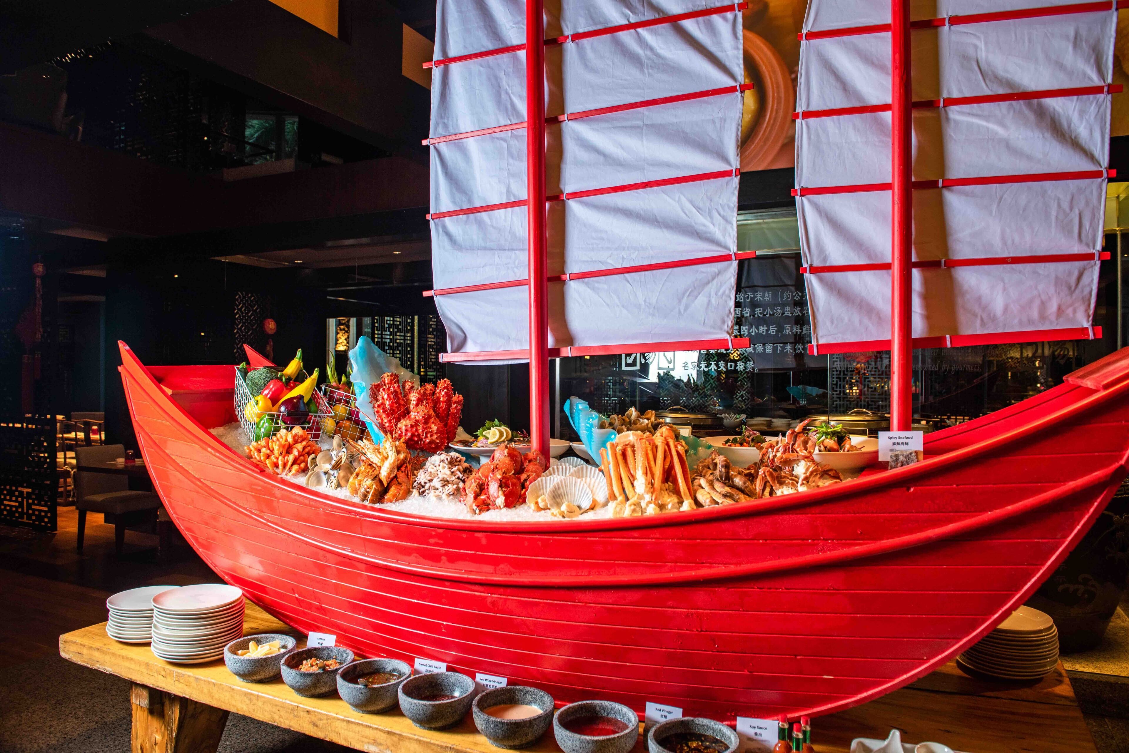 A red boat-shaped buffet with various seafood dishes and condiments.