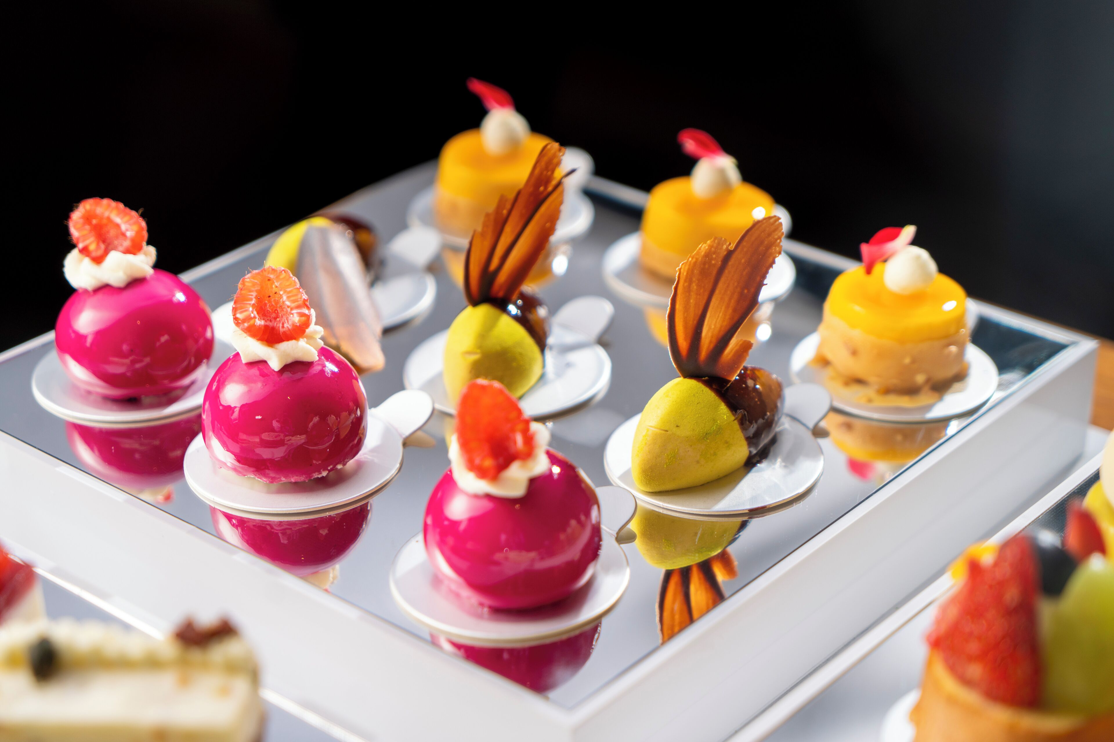 A variety of colorful desserts arranged on a reflective surface.