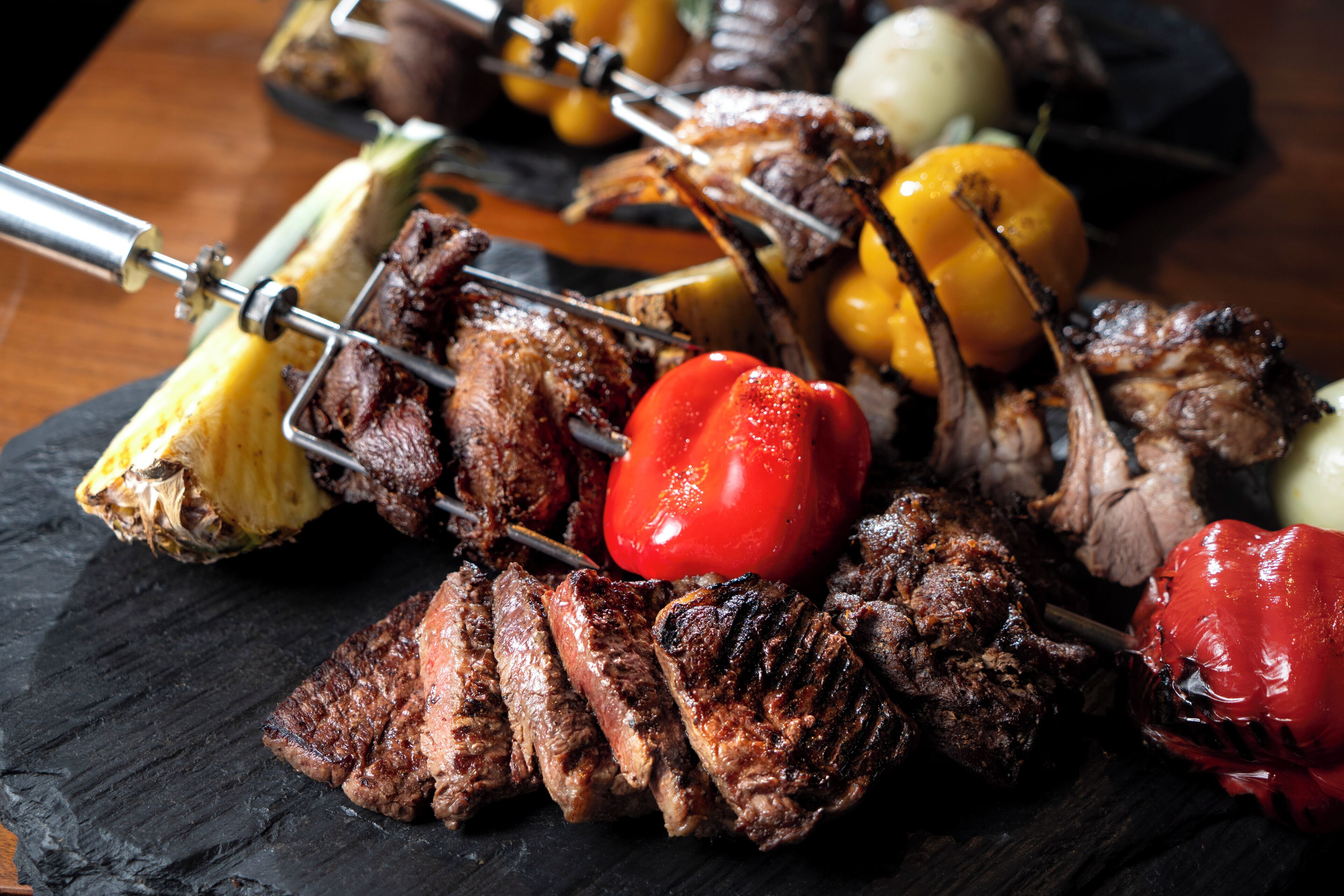 Un assortiment de viandes et de légumes grillés, présentés sur des brochettes et servis sur une assiette en ardoise noire.